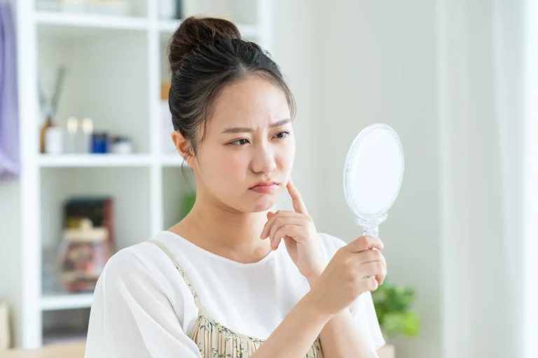 手鏡を見ながら頬に指を当て、肌の状態を気にする女性